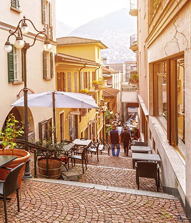 Narrow street with cafes and restaurants in the old town of Lugano (by MarinaDa)