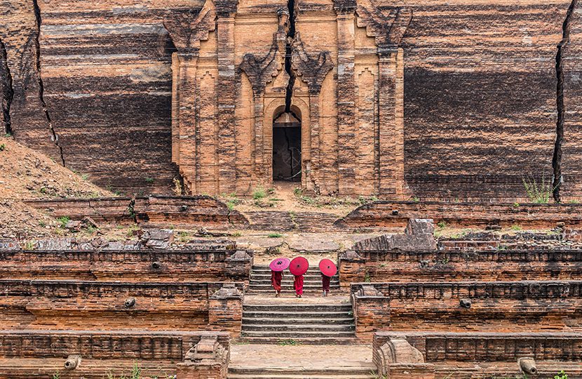 Three Buddhist novice are walking and holding the red umbrella at Mingun Pahtodawgyi, Bagan, Mandalay
