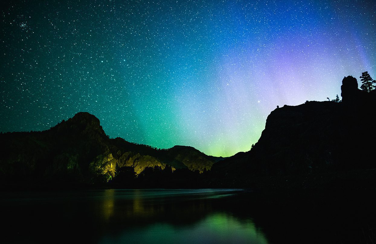 Aurora Borealis shining over mountains and reflecting on the Missouri River in Cascade by The Adaptive