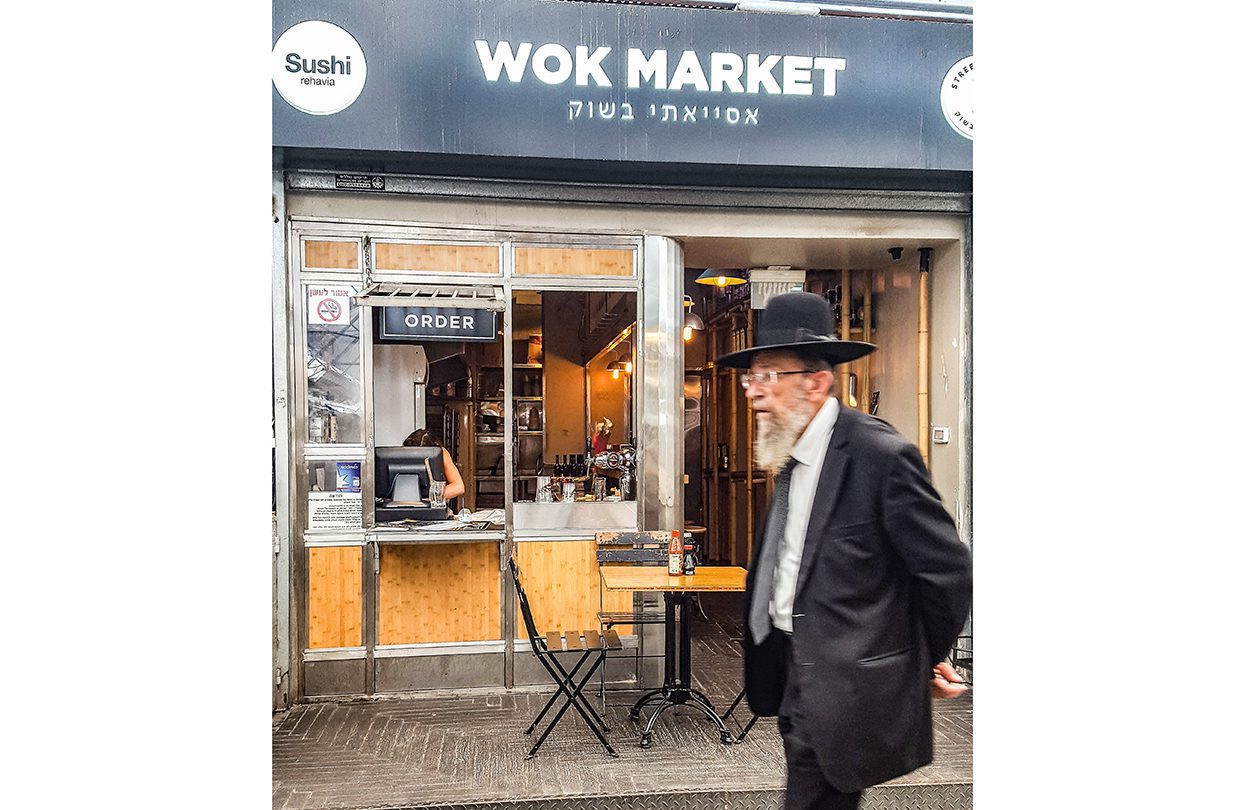 An old man passes a new Asian restaurant in Machne Yehuda