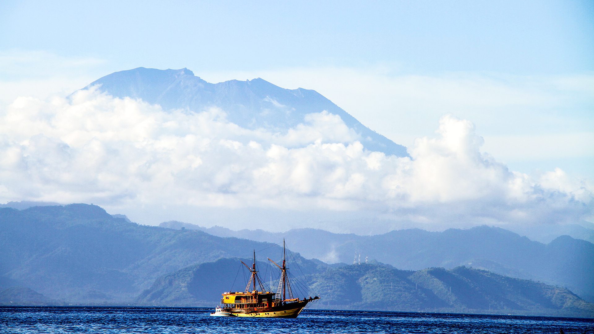 A liveaboard Penesi sailing ship cruises the waters off Nusa Lembongan in the shadow of the mighty Mt Agung