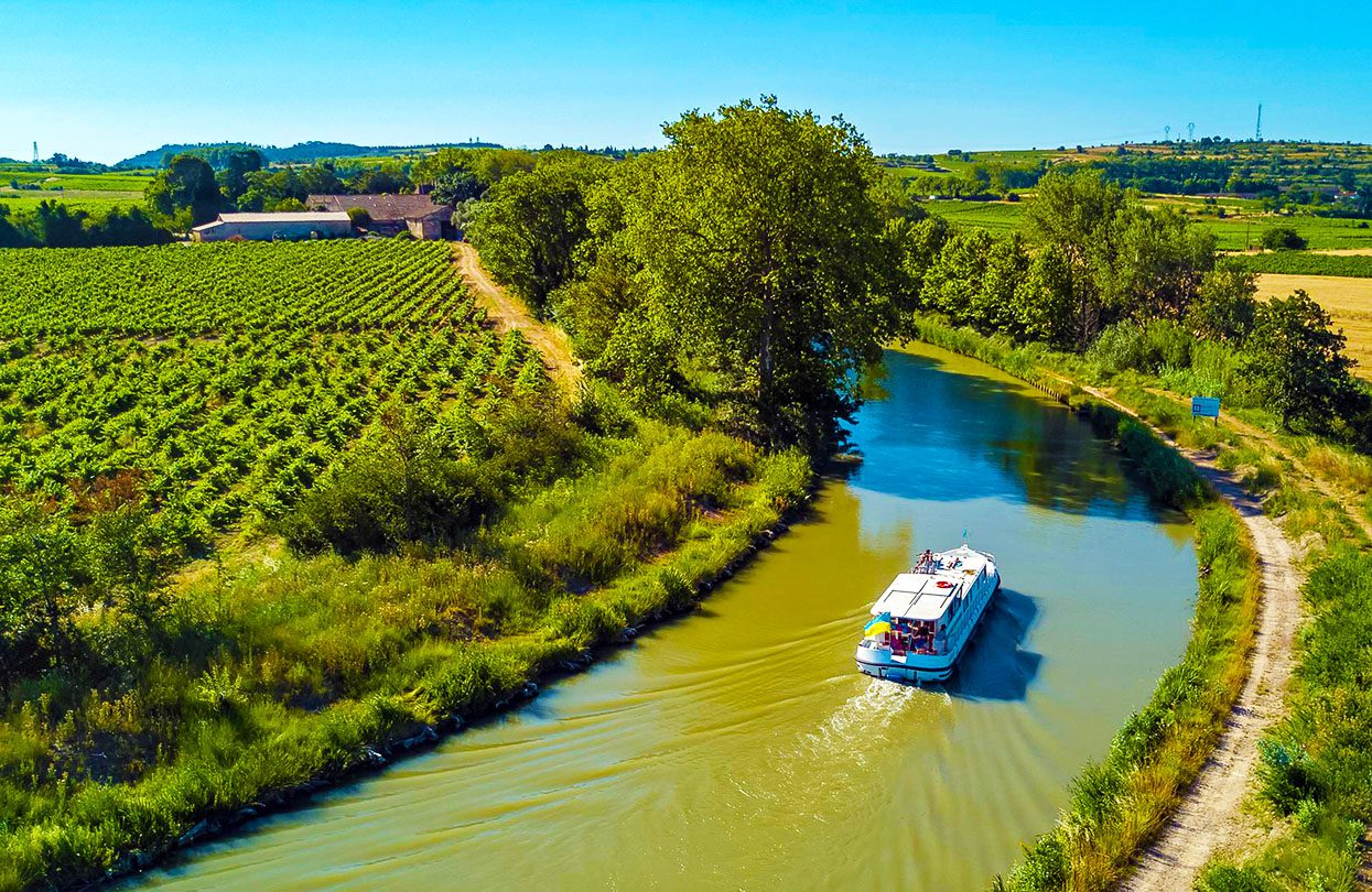 Aerial top view of boat in Canal du Midi from above, family travel by barge and vacation in Southern France, photo by JaySi, shutterstock